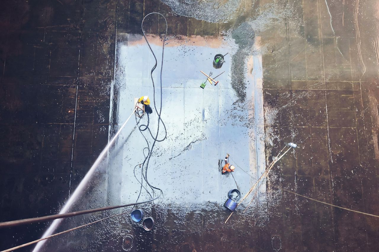Top view of workers cleaning a large surface with equipment and water hoses.