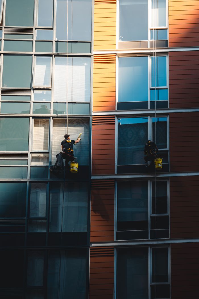 project-01-c Two workers hanging to clean windows on a modern skyscraper facade.