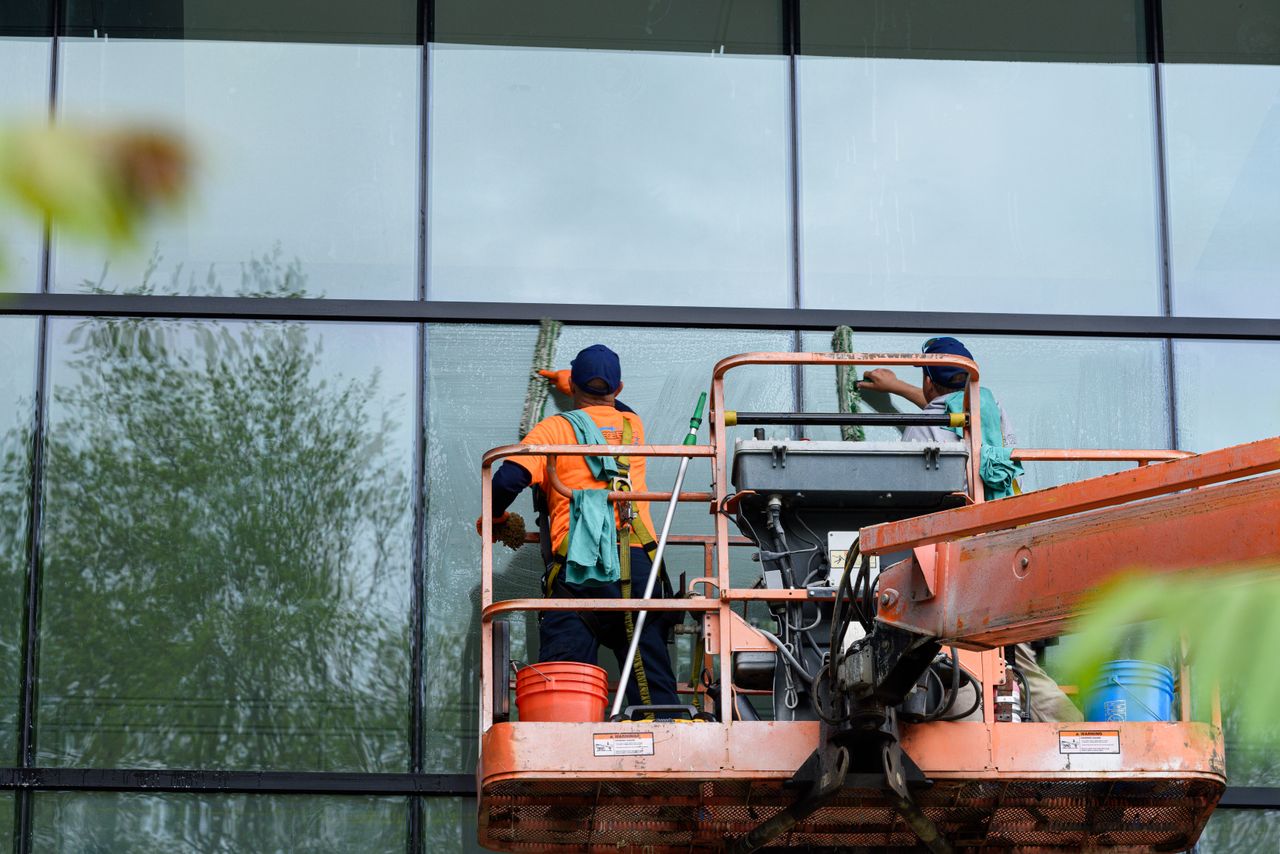 project-02-b Two workers cleaning windows on a glass building facade using a lift platform, enhancing building aesthetics.