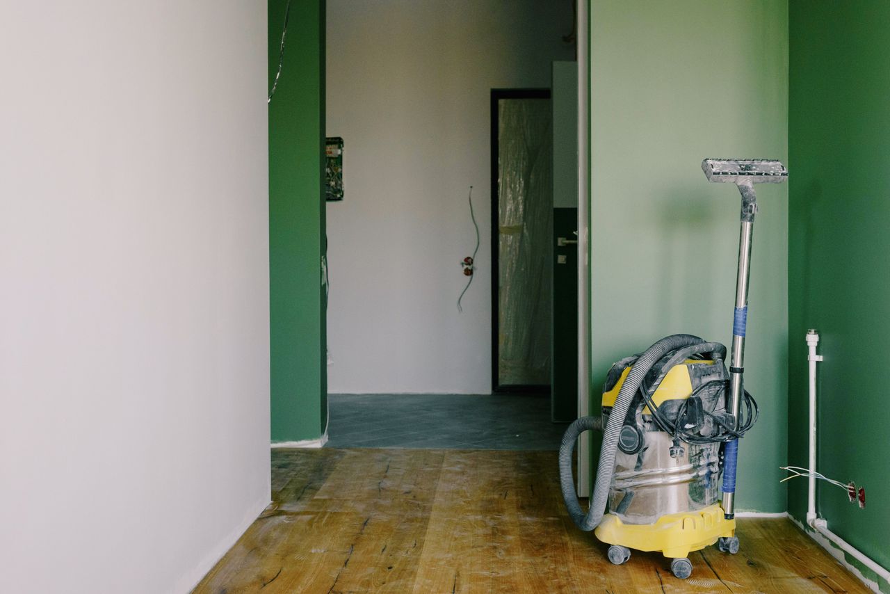 services-02 Industrial vacuum cleaner placed on dirty parquet in room with green walls and doorway in spacious apartment during repair works